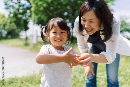 A mother and daughter share a joyful moment outdoors, with the child's hands held gently by her mother.