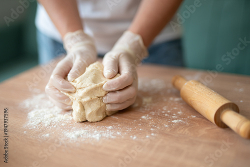 Hands in gloves kneading fresh dough on a floured wooden table