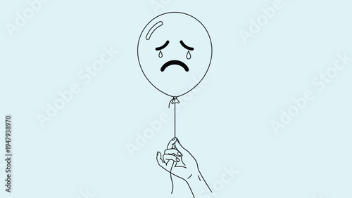 Human hand holding the string of a white balloon with a sad crying face drawn on it against a light blue background.