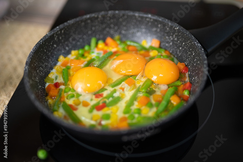 Fotografie Three fried eggs with mixed vegetables cooking in a frying pan
