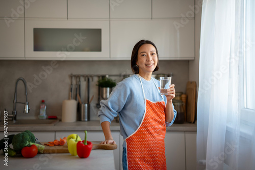 Fotografie Smiling woman hydrating preparing healthy vegetables in modern kitchen