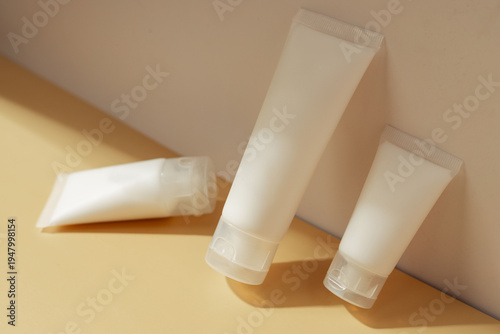 Minimal cosmetic tubes with skincare cream on pastel background in warm sunlight, beauty product packaging concept