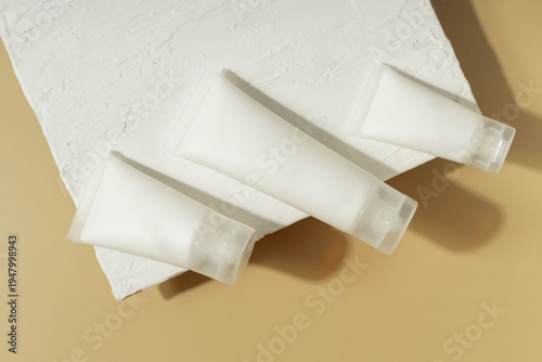 Minimal cosmetic skincare tubes on textured white surface with warm sunlight and shadows, beauty packaging concept