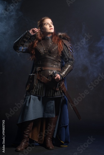 A warrior woman stands confidently amidst swirling smoke, clad in detailed armor and a flowing blue cloak.