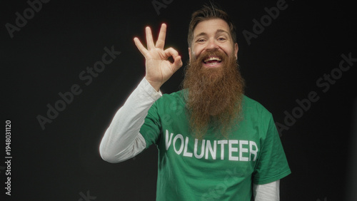 Canvastavla Man wearing green volunteer shirt making ok sign with a wide smile in a studio under soft lighting; approval