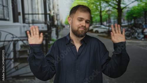фотографія Man shrugging with palms up and tilted head on a cobblestone city street, wearing navy button shirt and beard; nonchalant acceptance