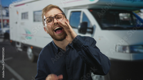 Man cupping hand to mouth shouting beside a camper van on a street, wearing glasses and a navy shirt; road trip excitement.