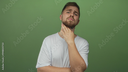 Foto Man wearing white tshirt with hand on chin touching beard in green studio; thinking doubt curiosity