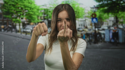 Obraz na plátně Woman flips middle finger on city street with blurred buildings under bright daylight; defiance