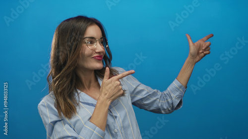 Foto Brunette woman with outstretched arms makes finger pointing gesture in bright blue studio; playfulness