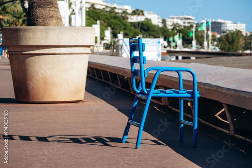 Bright blue metal chair casting a long shadow on sunlit pavement along the Croisette promenade in Cannes
