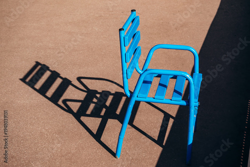 Bright blue metal chair casting a long shadow on sunlit pavement along the Croisette promenade in Cannes