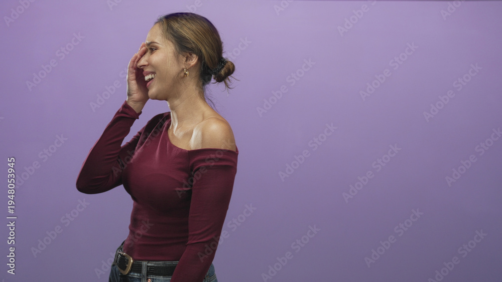 Fototapeta premium Woman laughing with hand covering one eye and exposed shoulder in purple studio setting; joy playful.