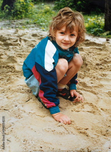 Little girl playing in sand, nostalgic 1990s childhood sandbox moment, vintage family snapshot