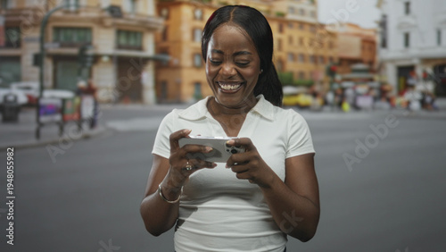 Woman smiling and tapping smartphone screen while holding phone horizontally on a busy city street with buildings and pedestrians; joy leisure.