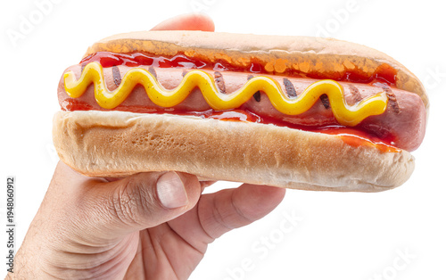 Classic American hot dog with a grilled sausage, ketchup and yellow mustard, served in a soft bun in a man's hand isolated on a white background.