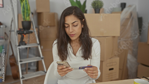 Tableau sur toile Woman holding smartphone and creditcard with hands visible while sitting among moving boxes in a building; budget planning focused