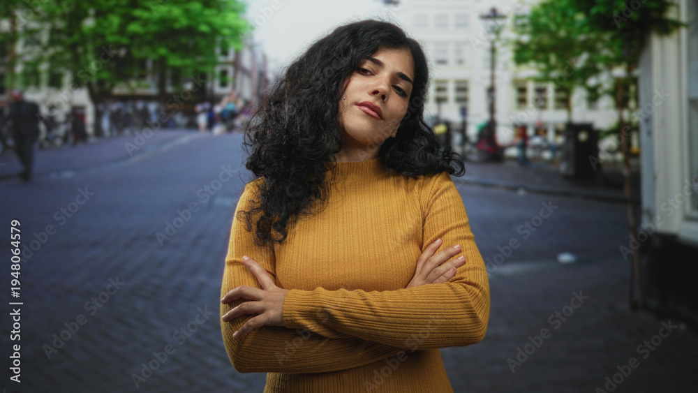 Fototapeta premium Woman with arms crossed, hands visible and closed eyes on a cobblestone street wearing mustard sweater and knitwear; quiet confidence.