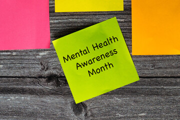 Four coloured sticky notes in the colours green, yellow, orange and pink on wooden styled surface. Green note says mental health awareness month