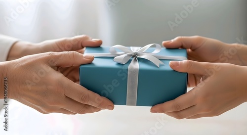 Close-up of hands exchanging a beautifully wrapped gift box with a silver ribbon, symbolizing a thoughtful present