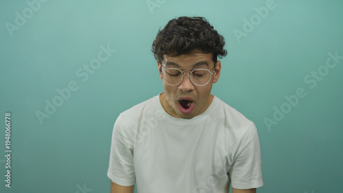 Bild auf Leinwand Man yawns showing mouth and glasses in studio setting on teal background under subtle soft light; fatigue