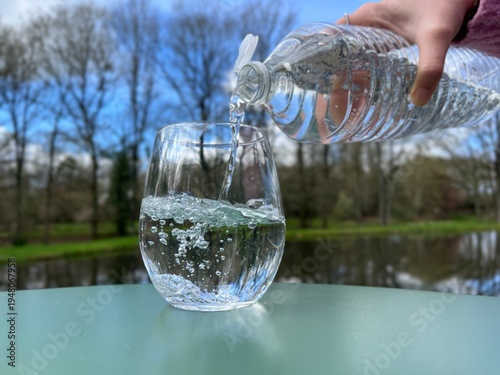 Obraz na płótnie Bouteille versant de l’eau dans un verre avec paysage en arrière-plan – hydratat