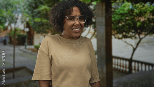 Obraz na plátne Woman grimaces on city street with leafy trees and lush foliage visible while wearing clear glasses; disgust