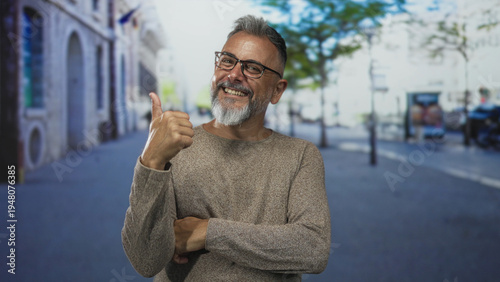 Фотография Man with gray beard and glasses smiling with arms crossed on a busy city street lined with buildings and trees; confidence approachability