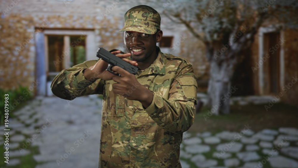 Fototapeta premium Man in camouflage uniform holds pistol and points gun with raised hand in building courtyard; tension duty.