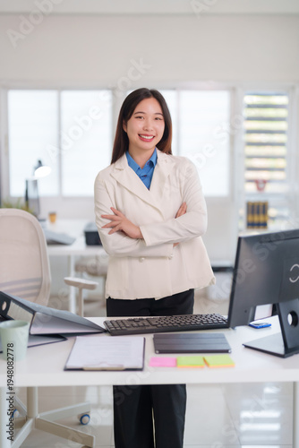 Asian adult woman professional standing smiling office workplace corporate business confident successful executive desk computer modern interior professional career