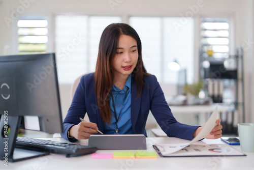 Asian adult businesswoman working office desk reviewing financial reports analyzing data using digital tablet productivity management corporate environment