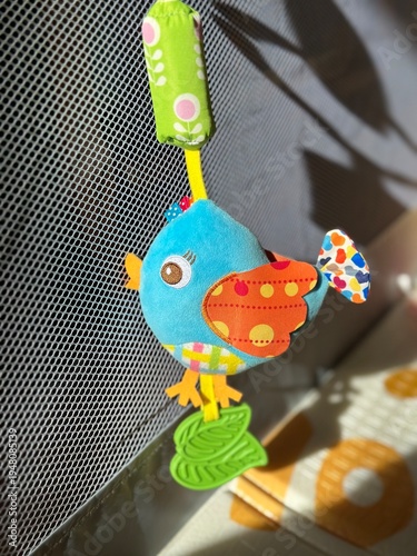 Wallpaper Mural A plush baby rattle toy shaped like a little bird hanging in a baby playpen, illuminated by bright sunlight. Torontodigital.ca