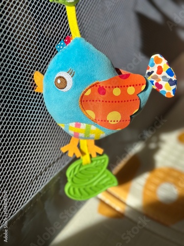Wallpaper Mural A plush baby rattle toy shaped like a little bird hanging in a baby playpen, illuminated by bright sunlight. Torontodigital.ca