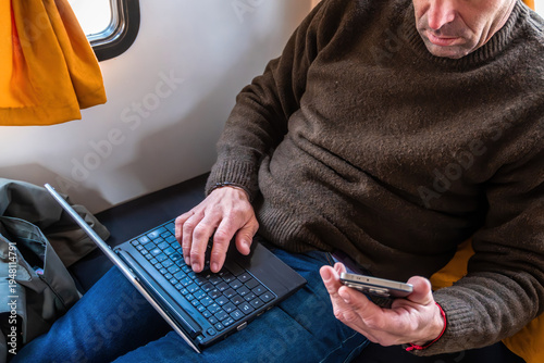 Man using laptop and smartphone while traveling, working remotely during a journey by train. Digital nomad concept