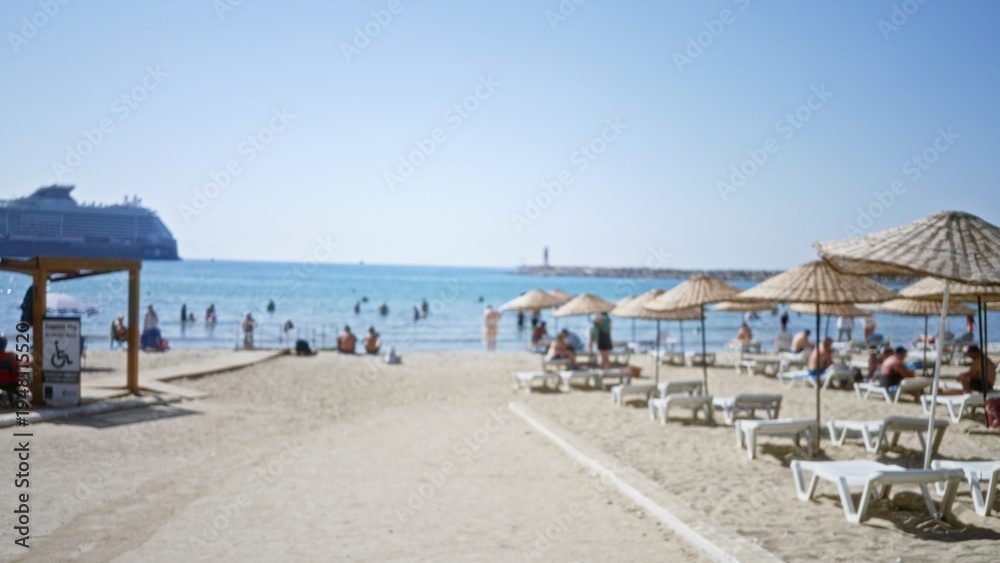 Obraz premium Defocused beach scene with umbrellas, loungers and distant cruise ship in soft outdoor background; background backplate copyspace calm.