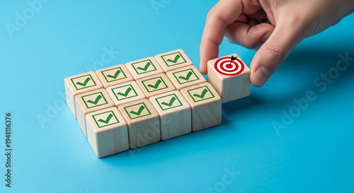 A hand places a wooden block with a target image among blocks with check marks on a blue background for task management, strategic planning, and project milestones