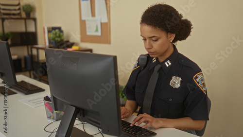 Fotografi Hispanic woman officer in uniform working indoors at a police station office focused on computer tasks