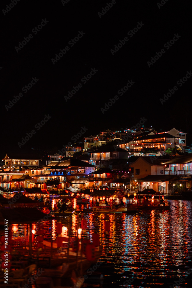 Fototapeta premium Chinese Style Lakeside Village Illuminated with Warm Lantern Lights Reflecting on Dark Lake at Night, Ban Rak Thai
