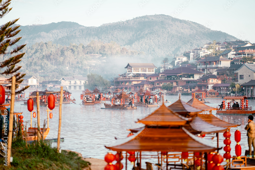 Obraz premium Crowded Wooden Boats with Red Lanterns on Misty Morning Lake with Chinese Village and Mountain Backdrop, Ban Rak Thai