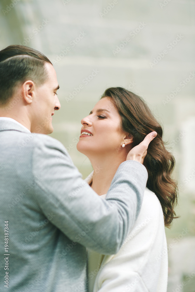 Fototapeta premium Romantic couple close portrait outdoors with man gently touching woman hair, elegant bride and groom sharing intimate moment during wedding day in charming European town