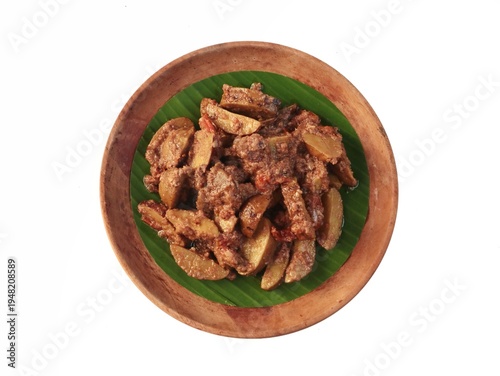 Indonesian spicy jengkol stew or semur jengkol served on a wooden plate with banana leaf on white background