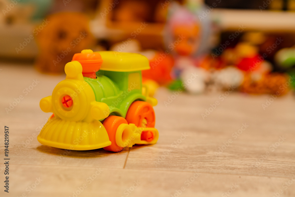 Fototapeta premium Small plastic toy train on floor. Colorful toddler engine model for imaginative play. Childhood development object for nursery school and home activity. Cute miniature transport vehicle.