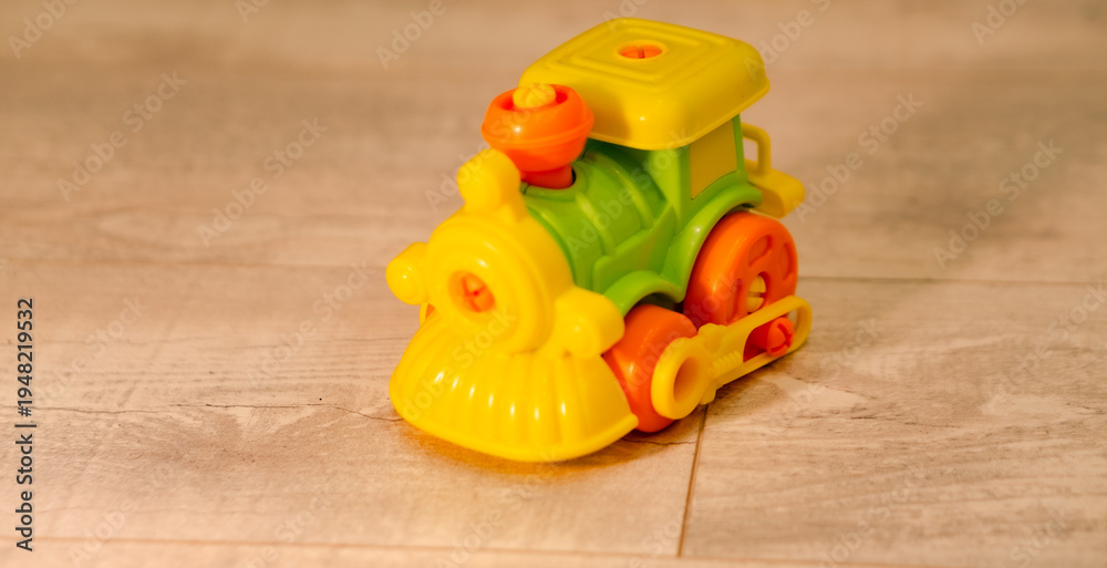 Fototapeta premium Small plastic toy train on floor. Colorful toddler engine model for imaginative play. Childhood development object for nursery school and home activity. Cute miniature transport vehicle.