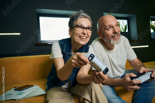 Joyful older couple playing video games in modern living room
