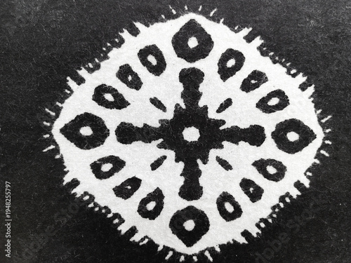 Close-up of a white circular ethnic motif printed on black fabric. High contrast textile texture with minimalist geometric design for fashion and decor background.