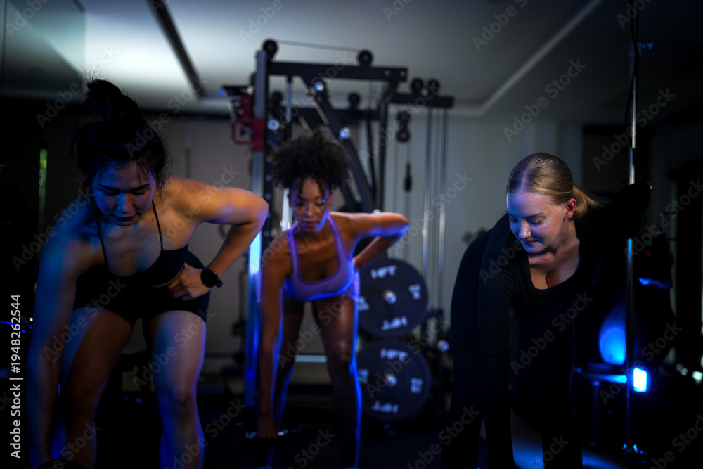Fototapeta premium Empowering diverse female athletes lifting weights under trendy blue neon lights. Focused on building sustainable metabolic health and physical endurance as a team.