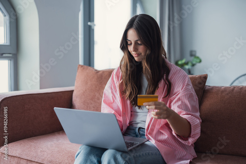 Foto Happy millennial woman sitting at home using her laptop to pay for products or s