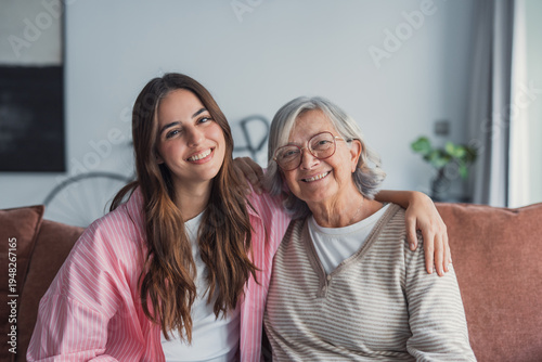 Bilde på lerret Senior woman and young adult woman sitting together on a sofa at home, smiling a