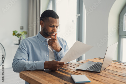 Foto Concentrated African American manager reading letter, paper handout, analyzing company statistics, thinking about financial risks, comparing results