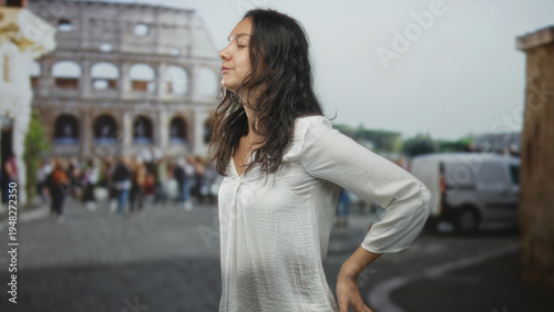 Photography Woman hand on hip posing on street near the colosseum in rome wearing a white blouse; calm reflection